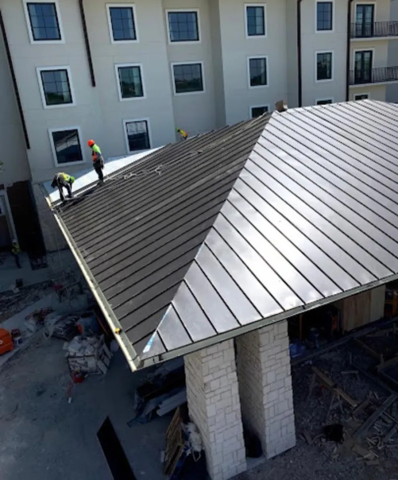 Crew installing standing seam metal roof panels on a commercial project in Winton